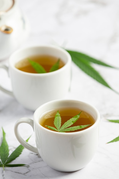 Dos tazas de té de cáñamo con hojas de cáñamo en suelo de mármol blanco