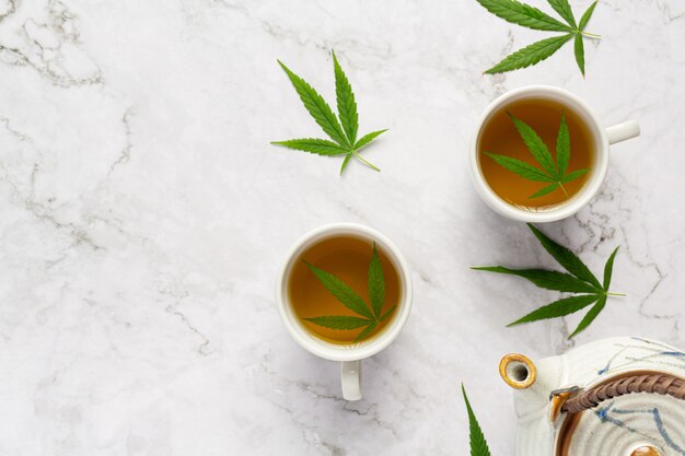 Dos tazas de té de cáñamo con hojas de cáñamo en suelo de mármol blanco