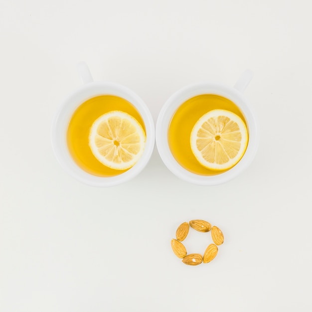 Dos tazas de té de jengibre con una rodaja de limón y almendras aisladas sobre fondo blanco