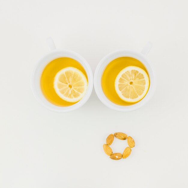 Dos tazas de té de jengibre con una rodaja de limón y almendras aisladas sobre fondo blanco