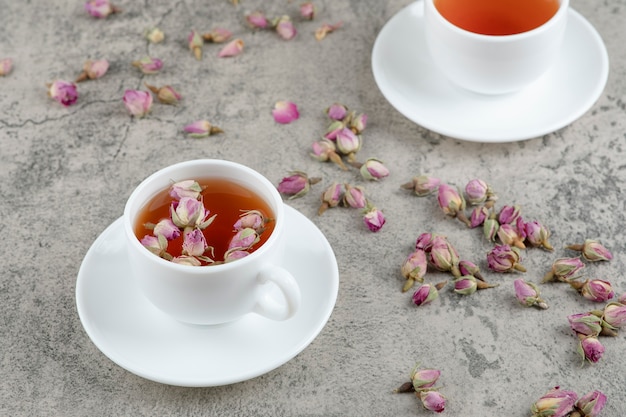 Dos tazas de té negro con flores secas sobre mármol.