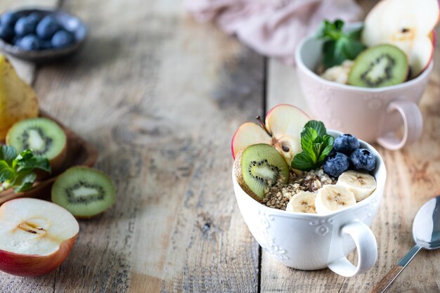 Dos tazones de avena o granola con arándanos, manzana, miel y menta sobre un fondo rústico de madera