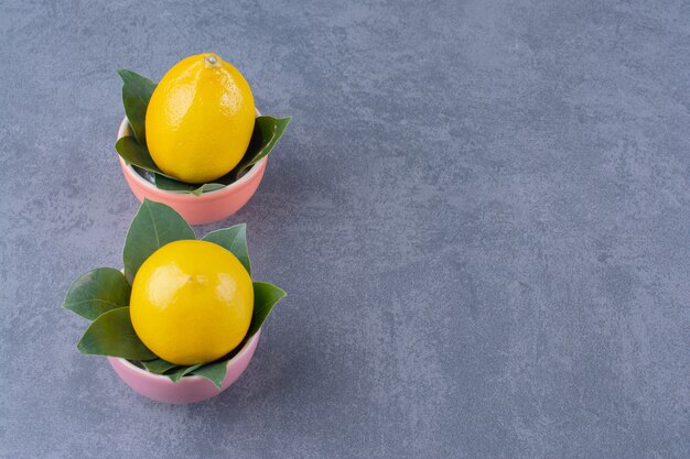 Dos tazones de limones maduros con hojas, sobre la superficie oscura