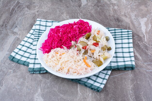 Dos tipos de chucrut y encurtidos en un plato blanco con mantel.