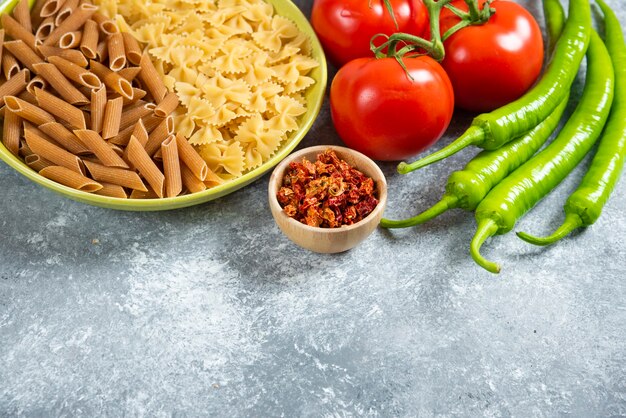 Dos tipos de pasta cruda en placa verde con verduras frescas.