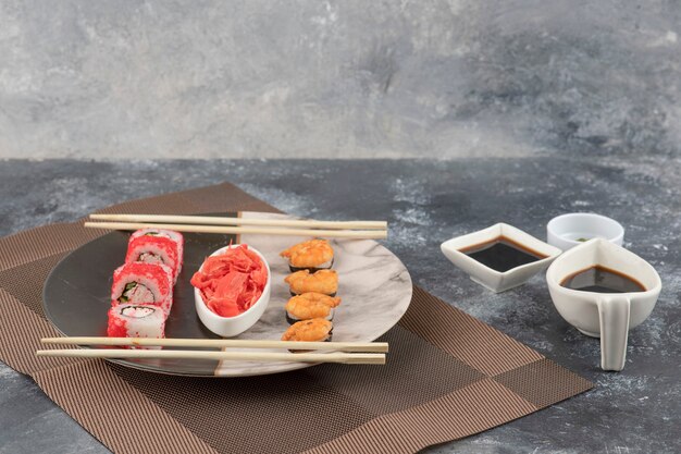 Dos tipos de sabrosos rollos de sushi en placa de mármol con salsa de soja