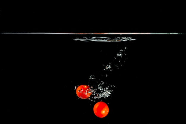 Dos tomates rojos cayendo en el agua contra el fondo negro