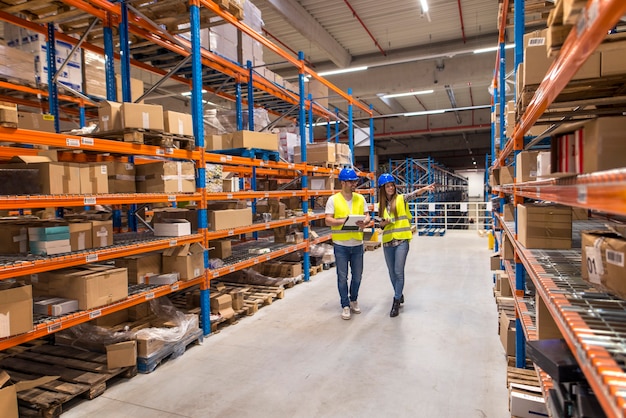 Dos trabajadores del almacén caminando en el área de almacenamiento de distribución discutiendo sobre logística y organización