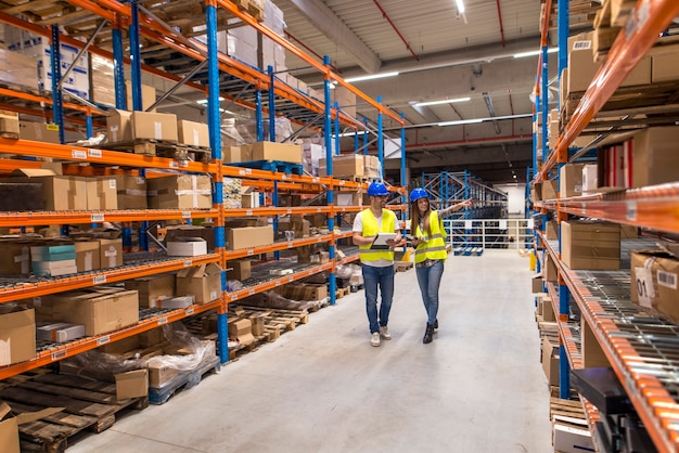 Foto gratuita dos trabajadores del almacén caminando en el área de almacenamiento de distribución discutiendo sobre logística y organización