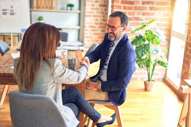 Foto gratuita dos trabajadores de negocios de mediana edad sonriendo felices y confiados trabajando juntos con una sonrisa en la cara estrechando la mano en la oficina