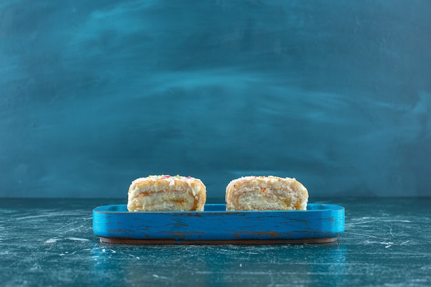 Dos trozos de pastel de rollo en placa de madera, sobre fondo azul. Foto de alta calidad