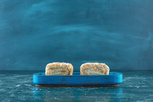 Dos trozos de pastel de rollo en placa de madera, sobre fondo azul. Foto de alta calidad