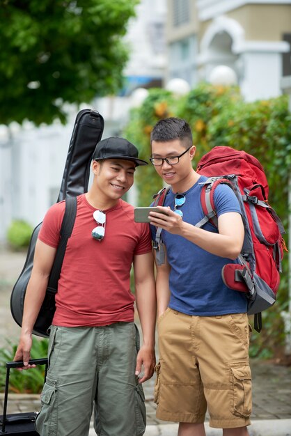 Foto gratuita dos turistas asiáticos masculinos mirando el teléfono inteligente en la calle de la ciudad