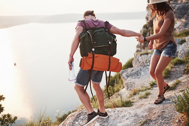 Dos turistas hombres y mujeres con mochilas suben a la cima de la montaña y disfrutan del amanecer.