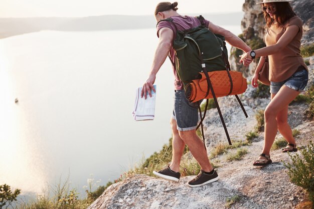 Dos turistas con mochilas suben a la cima de la montaña y disfrutan del amanecer
