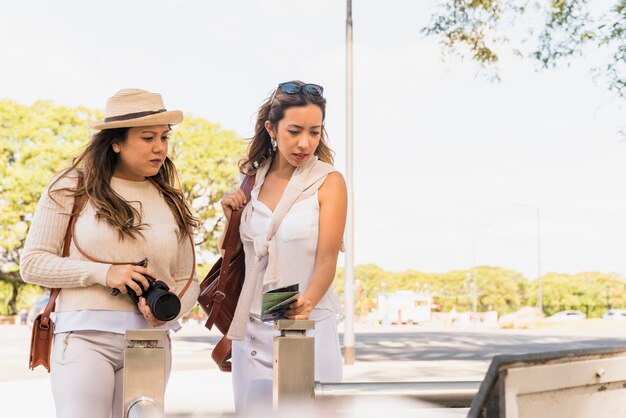 Dos turistas mujeres jóvenes mirando placa de información en el parque