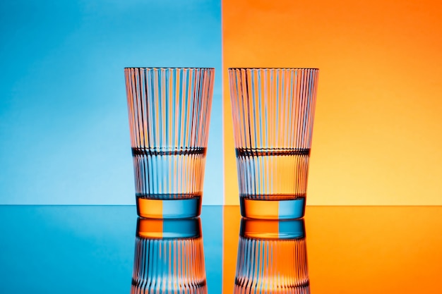 Foto gratuita dos vasos con agua sobre fondo azul y naranja.