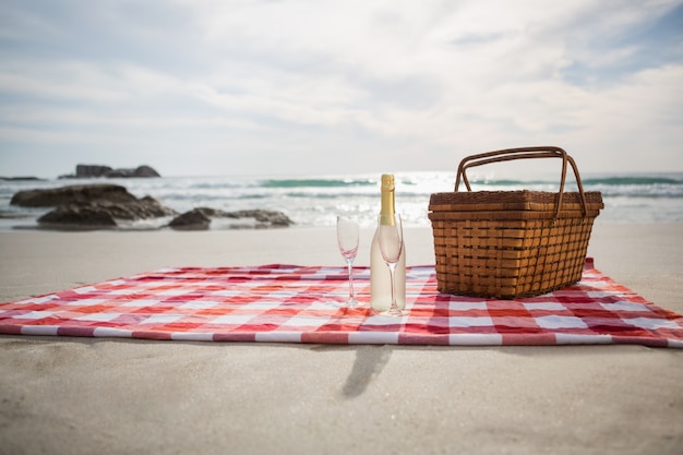 Foto gratuita dos vasos, una botella de champán y cesta de picnic en la playa manta