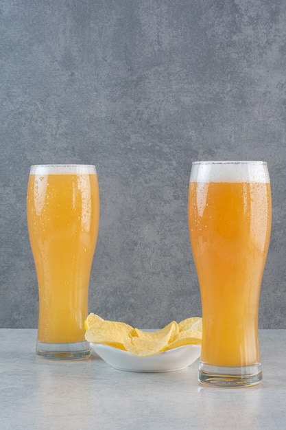 Dos vasos de cerveza con papas fritas en gris.