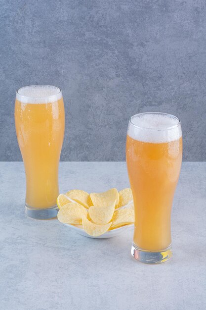 Dos vasos de cerveza con papas fritas en superficie gris