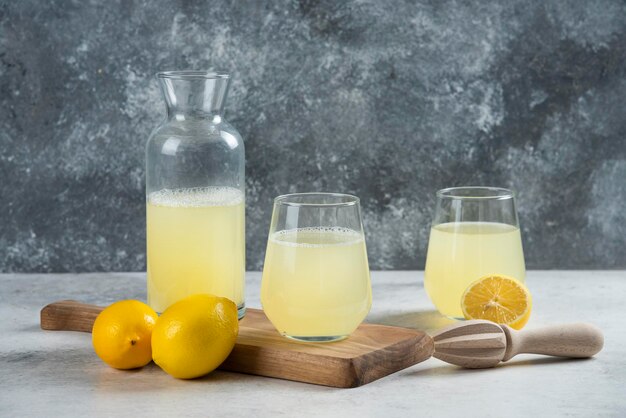 Dos vasos de jugo de limón y un tarro sobre una tabla de madera.