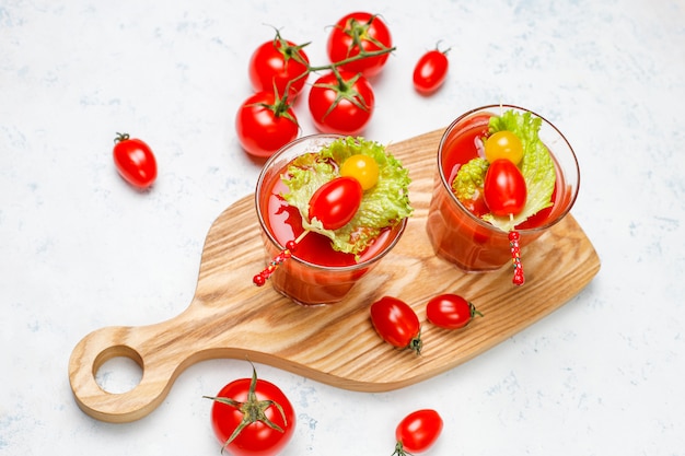 Dos vasos de jugo de tomate fresco y tomates en superficie de hormigón gris