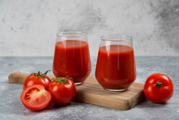 Dos vasos de jugo de tomate sobre una tabla de madera.