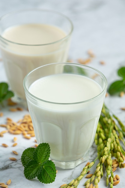 Dos vasos de leche de arroz con semillas de arroz y plantas de arroz sobre suelo de mármol blanco