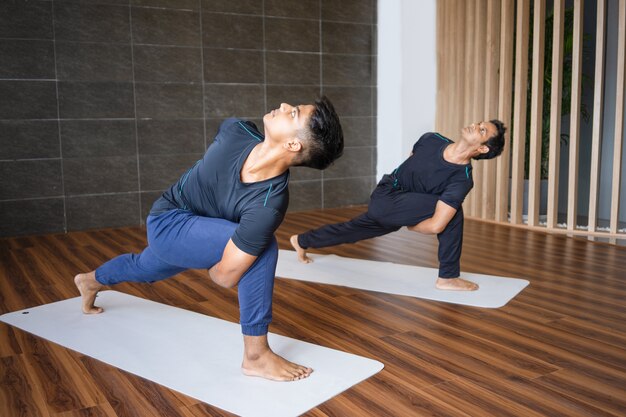 Dos yoguis haciendo una postura de ángulo lateral girado en el gimnasio