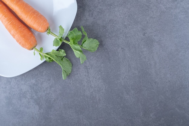 Dos zanahorias en un plato, sobre la superficie de mármol.