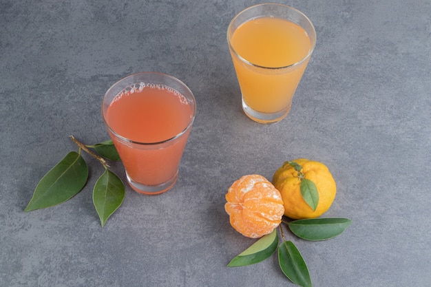 Dos zumos de frutas frescas con hojas y mandarinas.