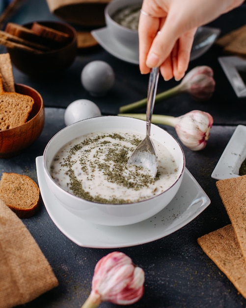 Foto gratuita dovga de yogur con verduras dentro de un plato blanco redondo junto con panes de pan huevos en mesa gris