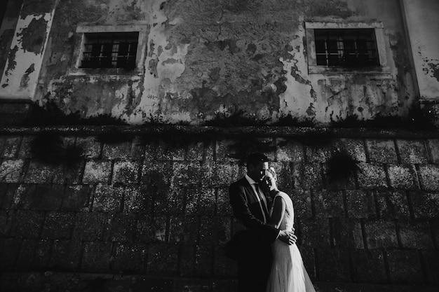 Dramática foto en blanco y negro de novios posando delante de un muro de piedra