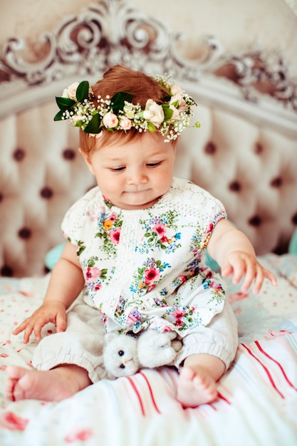 Dreamy niña en corona de rosas se sienta en la cama de lujo suave