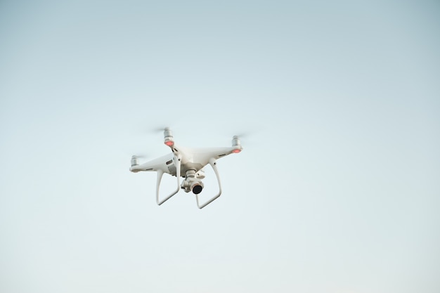 Drone blanco flotando en un cielo azul brillante