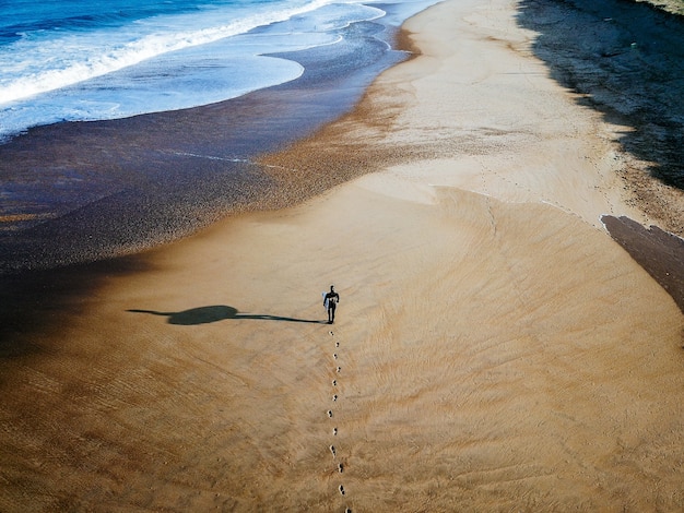 Drone Shot de Surfer caminando por la costa