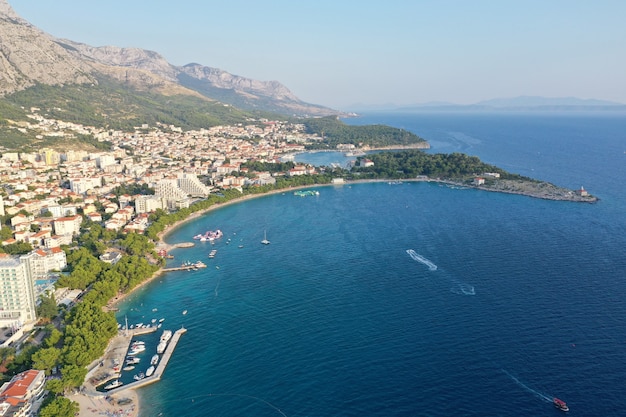 Drone vista de la ciudad de Makarska rodeada por el mar bajo un cielo azul y la luz del sol en Croacia