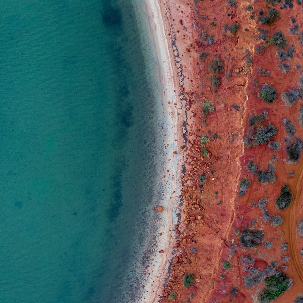 Drone vista del mar rodeado por la orilla cubierta de arena roja y piedras