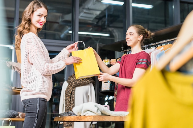 Dueño de la boutique dando una bolsa de papel amarilla a una joven sonriente