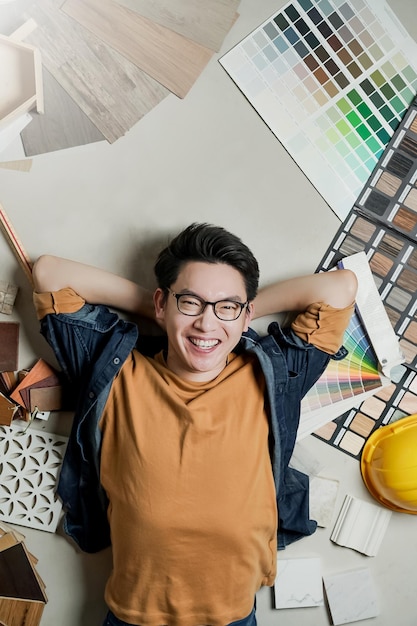 El dueño de la casa del hombre asiático de felicidad inteligente se acuesta en el piso con el marco de muestra del material de la casa en torno al concepto de ideas de renovación del hogar