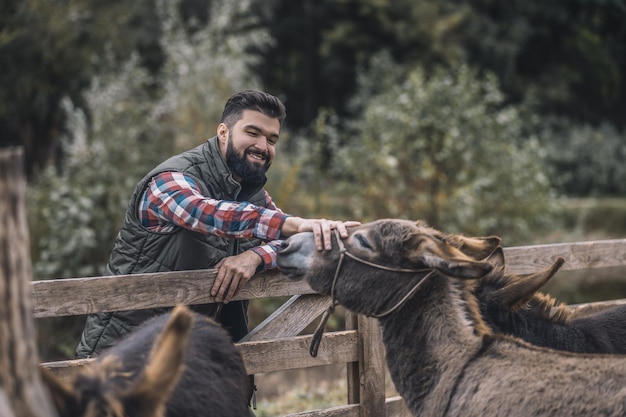 Foto gratuita dueño de la finca. joven agricultor de pelo oscuro de pie cerca del corral de ganado