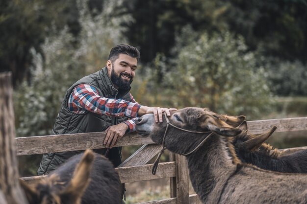 Dueño de la finca. Joven agricultor de pelo oscuro de pie cerca del corral de ganado