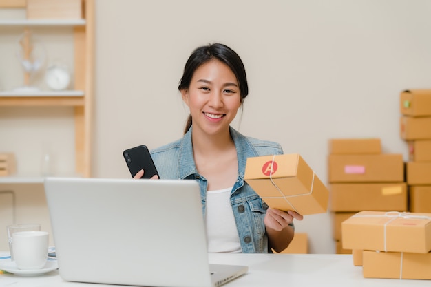 Dueño joven asiático elegante hermoso de la mujer de negocios del empresario de la PYME que comprueba el producto en el código común del qr de la exploración que trabaja en casa.