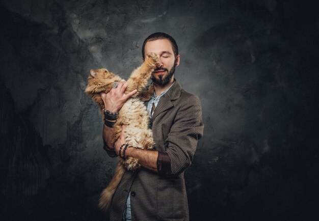 El dueño de la mascota en el blazer sostiene un gato grande y esponjoso en un estudio fotográfico oscuro.