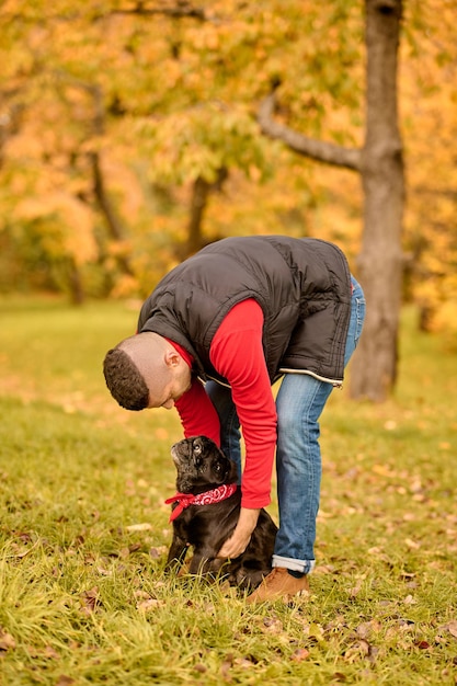 El dueño de una mascota con su amigo. Un hombre de pie en el parque y sosteniendo a su lindo perro.