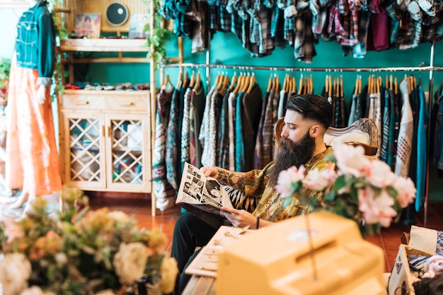 Dueño masculino de la tienda que se sienta en silla en su tienda de ropa