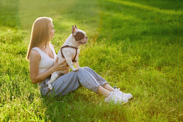 Dueño de perro hembra sosteniendo bulldog francés de rodillas al aire libre