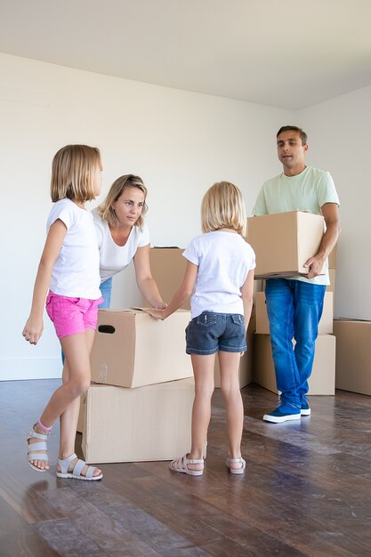 Dueños de casas nuevas felices con dos niños sosteniendo cajas de cartón y corriendo hacia la nueva casa