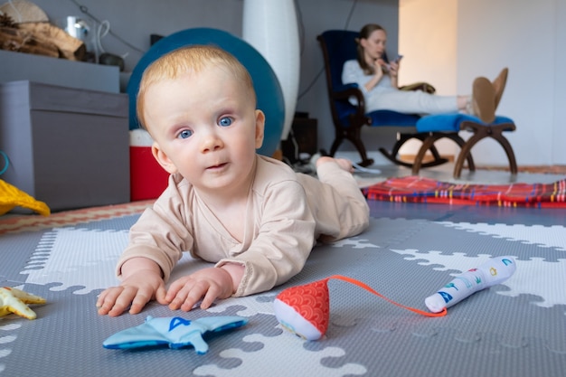 Dulce bebé de ojos azules jugando en el piso entre juguetes