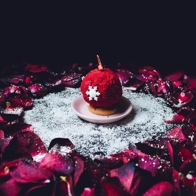 Dulce bola cubierta de polvo rojo se encuentra en el círculo de pétalos de rosas rojas